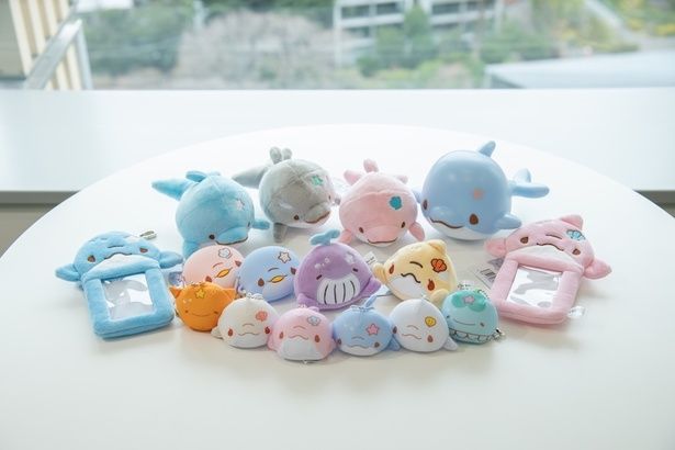 「ぬいぐるみ」(1870円/左奥)、「ルームランプ」(2980円/右奥)、「カードホルダー」(あおいるか・ぴんくいるか各1650円/両サイド)、「シリコンケース」(あおいるか・ぴんくいるか各1078円/中列左)、「フェイスマスコット」(くーみん・あるる各1320円/中列右)、「ビーズマスコット」(8種各990円/前列) 撮影＝小山志麻