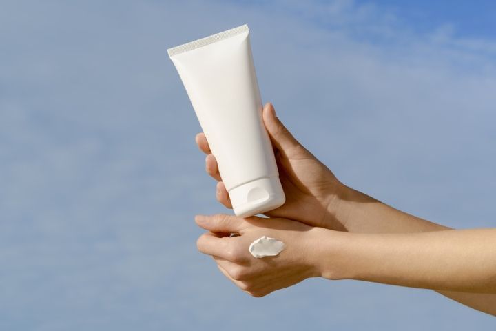 青空を背景に、汚れのついた女性の手が白いモックアップチューブを持っている。美容製品、顔と体のケアのコンセプト 日焼け止めイメージ