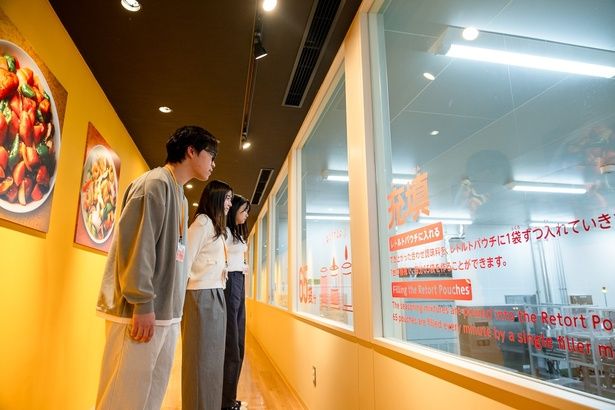  ガラス越しに、いつも食べている「Cook Do」が作られている工程を見学。思った以上に速く動いている機械に驚く3人