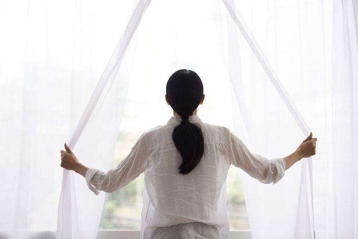 朝の光を入れるためにカーテンを開ける女性