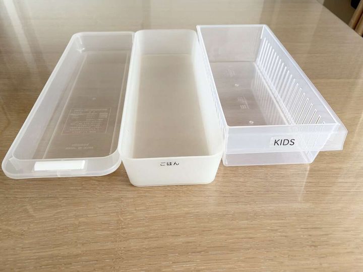 木のテーブルに並べられた透明と半透明の収納ケース3点（「ごはん」「KIDS」のラベル付き）