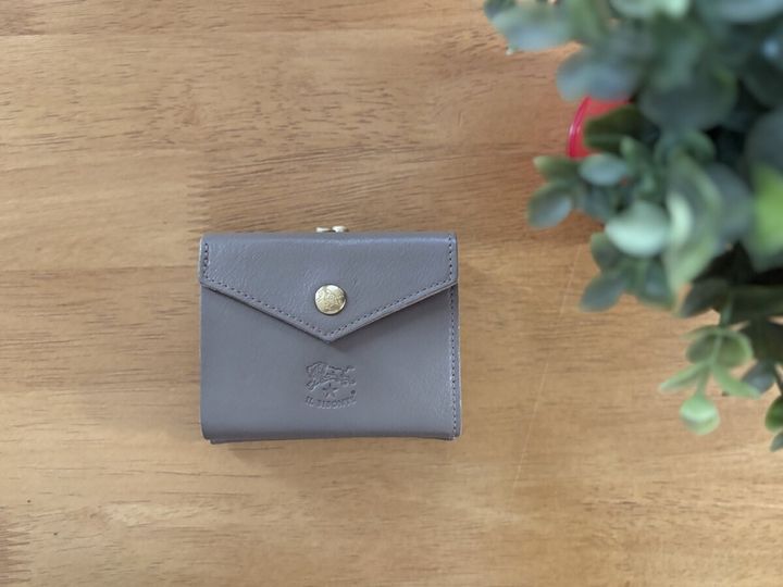 木目のテーブルに置かれたグレーの二つ折りレザー財布と観葉植物
