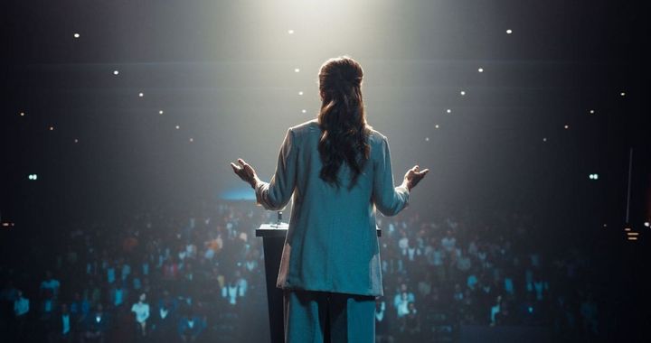 大会場の国際会議で壇上に立ちスピーチしている女性の後ろ姿