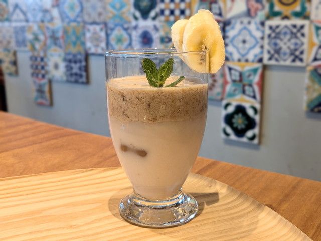 アーモンドミルクの上にコーヒーバナナのふわふわフォームがのった二層ドリンク。グラスにバナナスライスが飾られている