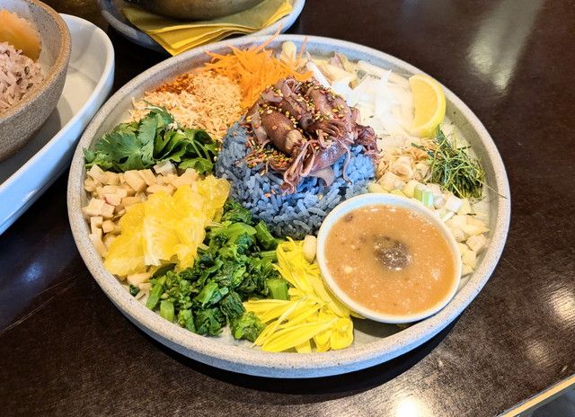 カラフルな野菜・ハーブ・ブルーライスが美しく盛られたカオヤム。中央にアーモンドミルクのタレが添えられている