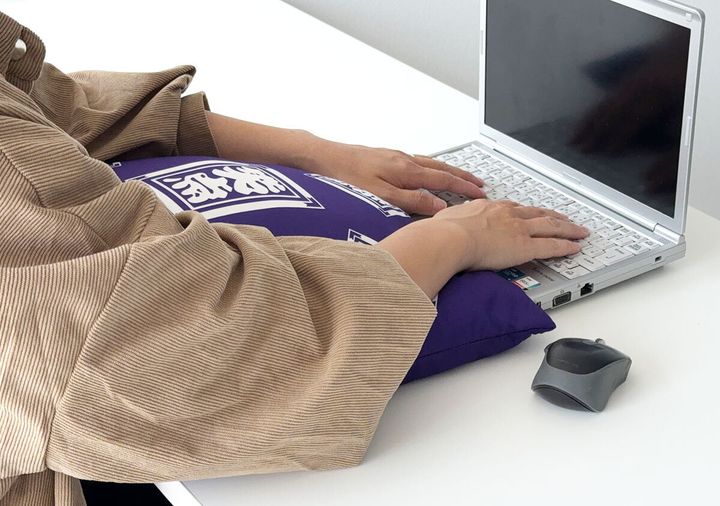 デスクに置いた笑点座布団クッションに腕を乗せてノートパソコンで作業する様子