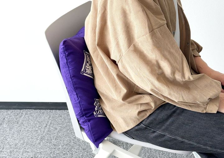 椅子の背もたれ部分に置いた笑点座布団クッションに腰をあずけて座る女性