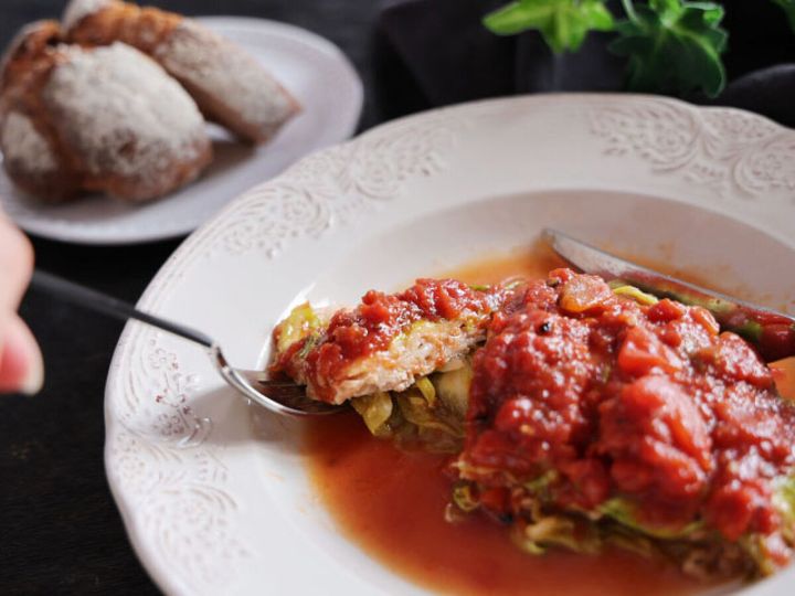 白い皿に取り分けた春キャベツと豚肉のトマトチーズ蒸しをスプーンですくう様子、横にパンが添えられている