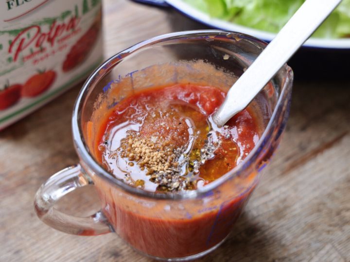 ガラスの計量カップの中でカットトマトに顆粒コンソメ・砂糖・オリーブオイル・黒こしょうを加え混ぜているトマトソース