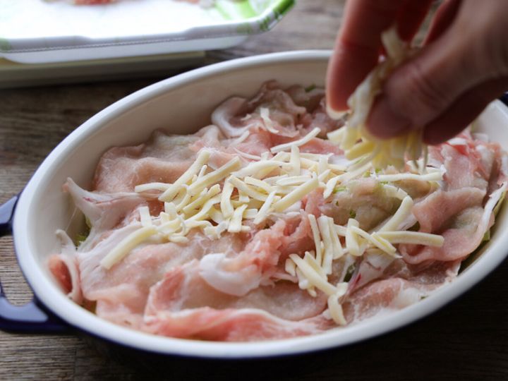 敷き詰めた薄切り豚肉の上にピザ用チーズを手で散らして広げている様子