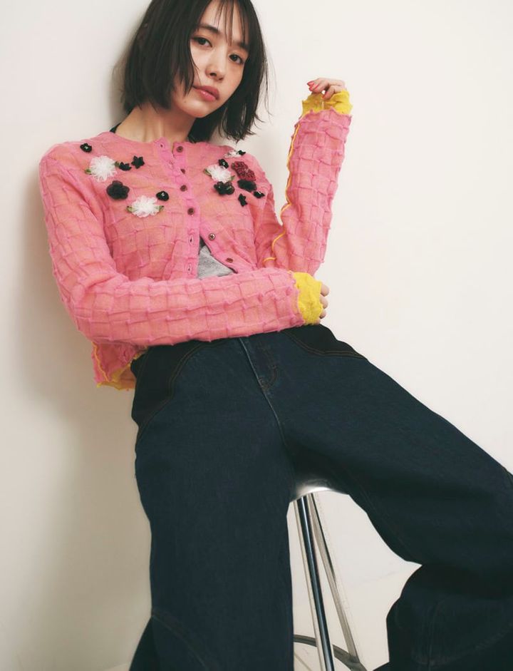 立体的なフラワーモチーフがついたピンクのカーディガンとデニムパンツを着た女性