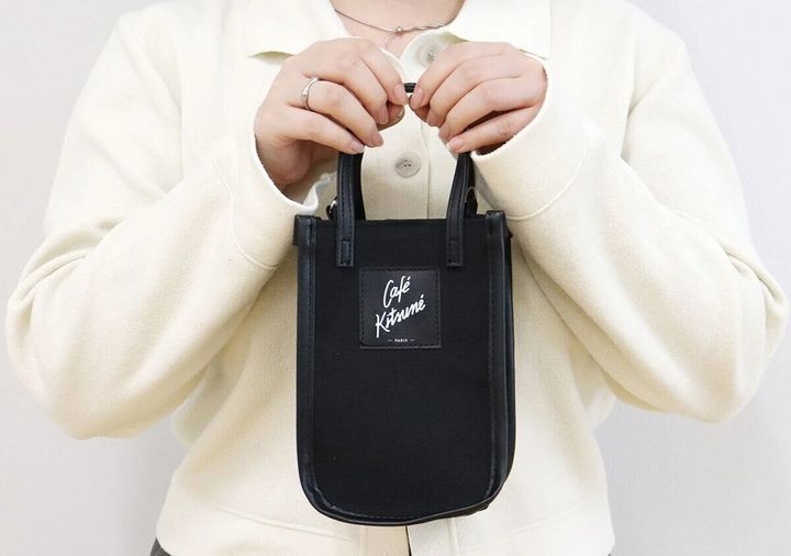 Café Kitsunéの黒スマホショルダーを白ジャケットの女性が両手で持つ様子