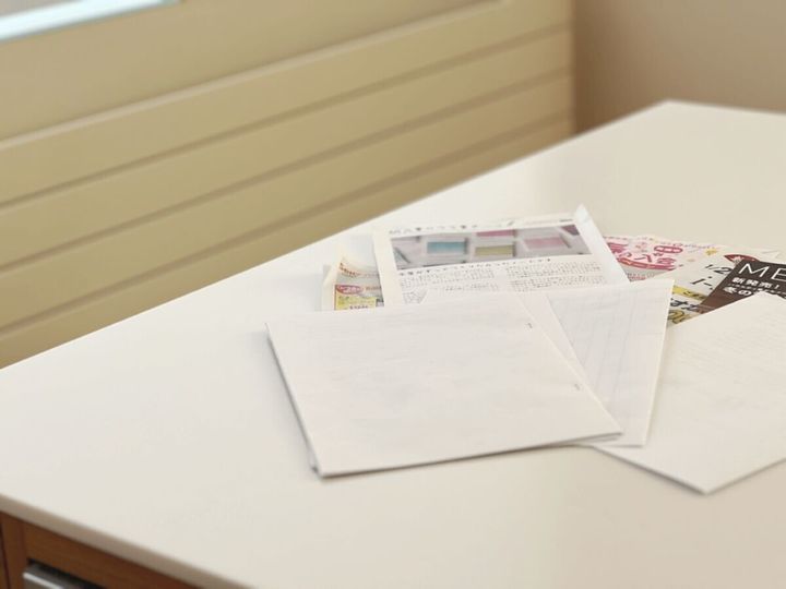 白いテーブルの上にチラシや手紙などの書類が散らかっているリビングの様子