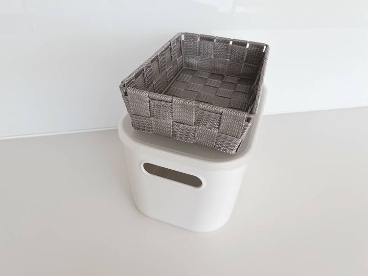 白い収納ボックスの上にグレーの編み込みバスケットが乗っているシンプルな収納アイテムの写真