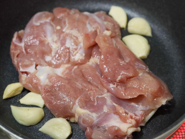 フライパンに鶏もも肉を皮目を下にして置き、まわりににんにくを散らした様子
