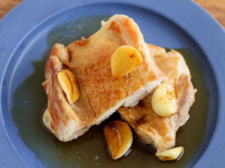 青い皿に切り分けて盛った鶏もも肉と焼きにんにく