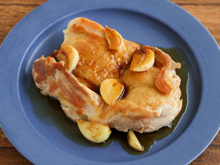 青い皿に盛った鶏もも肉と焼きにんにくにタレをかけた料理