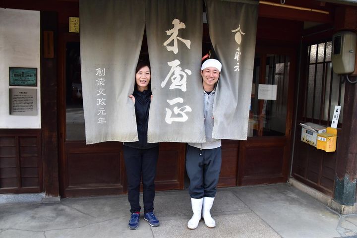 酒蔵の入口で、暖簾からひょっこり顔を出す大西さんと妻・香美さん