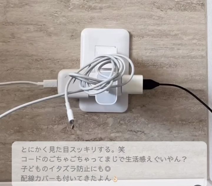 White wall outlet plate with a tangled bundle of charging cables, including a white USB-C/Lightning-style cable and a black power plug, resting on a light beige wall.