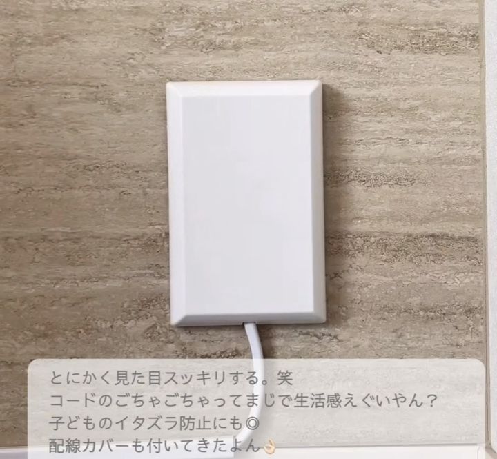 White rectangular wall plate with a cord coming out of the bottom, mounted on beige tile wall (cable management/hidden outlet setup).