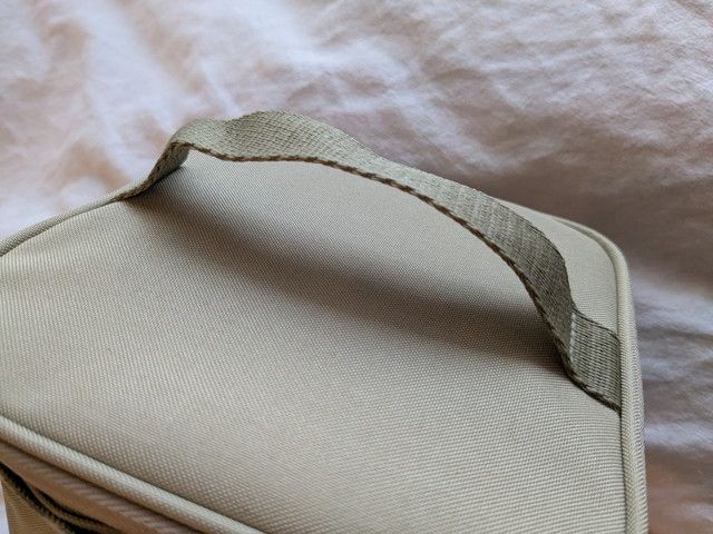 バニティポーチ上部のハンドルのアップ。ベージュのテープ素材のハンドルがついている