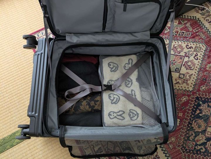 開いた黒いスーツケースに荷物が詰められた旅行グッズを出し入れする俯瞰写真