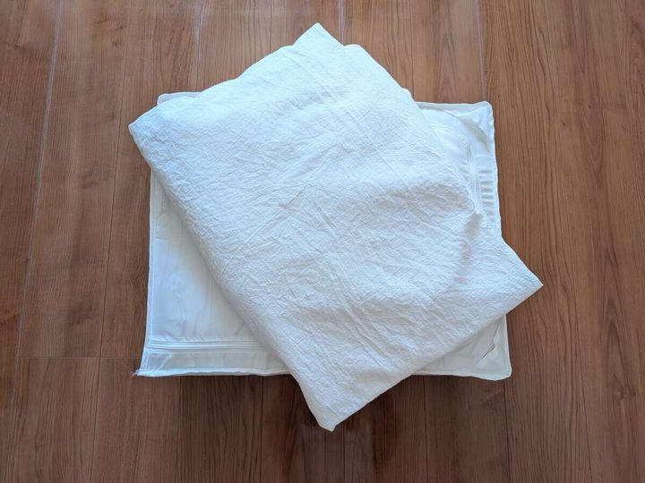 木目の床に置かれた白いシーツや寝具を片付けのため取り出した俯瞰写真