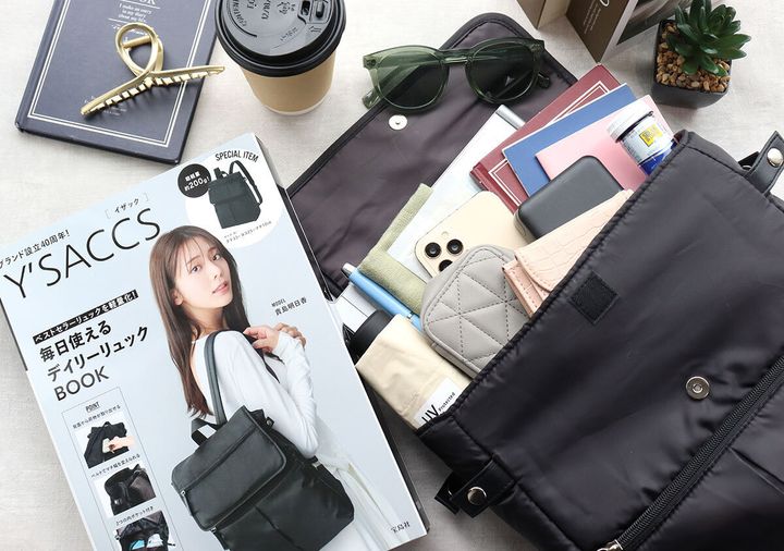 ムック本と荷物を入れたリュックを小物と並べて俯瞰で撮影した写真