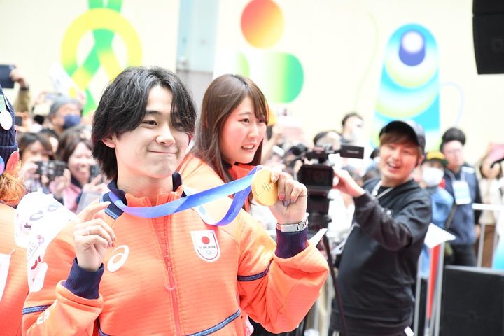 画像: 金メダルを掲げて、写真撮影のリクエストに応じる戸塚優斗選手（左）。パレード後の会見で「応援の声を実際に聞けて、こちらから感謝の意を込めてあいさつできてうれしかった。声援を滑りに変えて、五輪や今後の大会に全力で挑みたい」と思いを明かした。