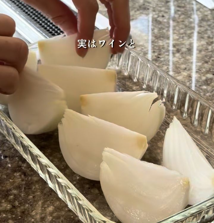 Hands slicing peeled white onions into wedges and placing them in a glass dish on a granite countertop.