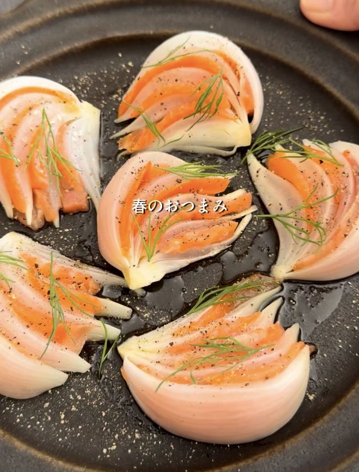 Onion petals wrapped around smoked salmon with dill, plated as a spring appetizer on a dark dish.