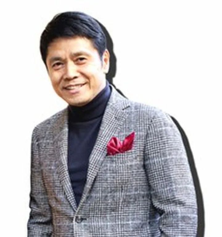 グレンチェックのジャケットに赤いポケットチーフを差した男性の上半身写真。審査員または関係者のプロフィール用とみられる人物ポートレート。