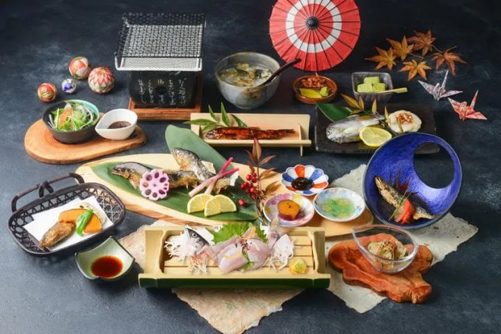 天然鮎の塩焼き・刺身・唐揚げ・お椀などを含む鮎料理フルコースの料理全体俯瞰写真。赤い和傘や紅葉の小道具とともに複数の器が並ぶ