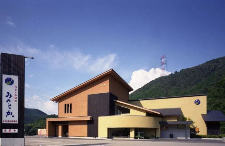 岐阜県郡上市の天然鮎専門店みやちかの店舗外観。山を背景に木目調と黄色の外壁が特徴的な現代和風建築で営業中の看板が見える