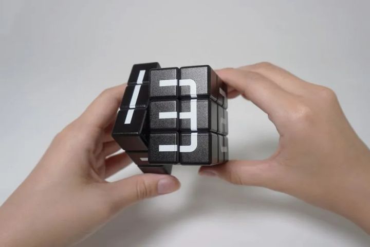 手に持ったモジキューブ黒。各面に文字を構成するためのパネルが並び、指でキューブを操作している様子