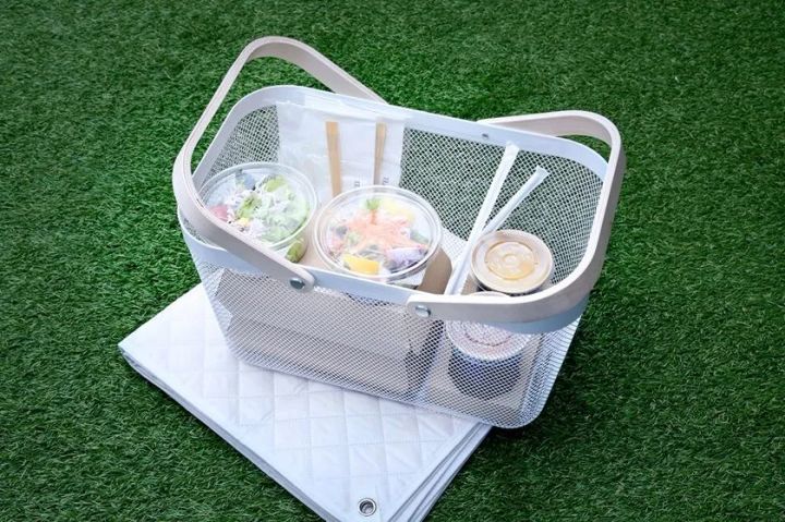 白いメッシュ素材のピクニックバスケットにサラダ・フルーツ・スープ容器と竹箸を収納し、折り畳みシートとともに芝生に置いた備品写真