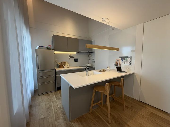 泉北ホームみのお第2展示場のアイランドキッチン。グレー系対面キッチンとカウンター席2脚、ステンレス冷蔵庫・木製ペンダントライトを備えたシステムキッチン全景