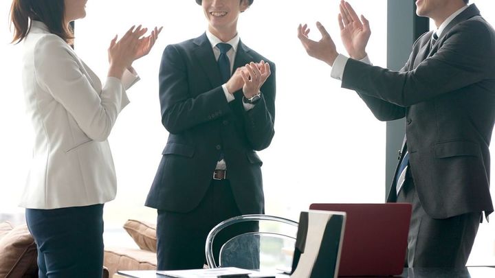 オフィスで手を叩きながら談笑するビジネスパーソンたち