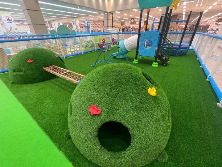 人工芝エリアに丸型草山クライミング遊具、木製ラダー、シーソー、青色立体遊具が並ぶ公園コーナー