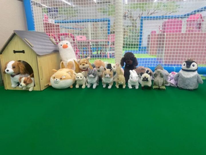 緑のカーペット上に犬、猫、うさぎ、ペンギンなど約15体の動物ぬいぐるみと木製犬小屋が並ぶ動物園コーナー