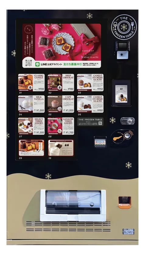 THE FROZEN TABLEの冷凍自動販売機全景。カヌレ・アイス・アソートなど10種のメニューパネルと各価格（900円〜1,700円）が表示され、LINEアカウントの案内も掲示されている
