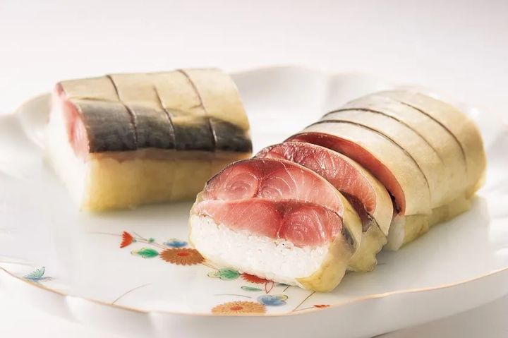 竹の皮で包んだ押し寿司2切れを白地の有田焼風皿に盛り付けた姿寿司。サバとマグロの断面から酢飯との重なりが確認できる商品写真