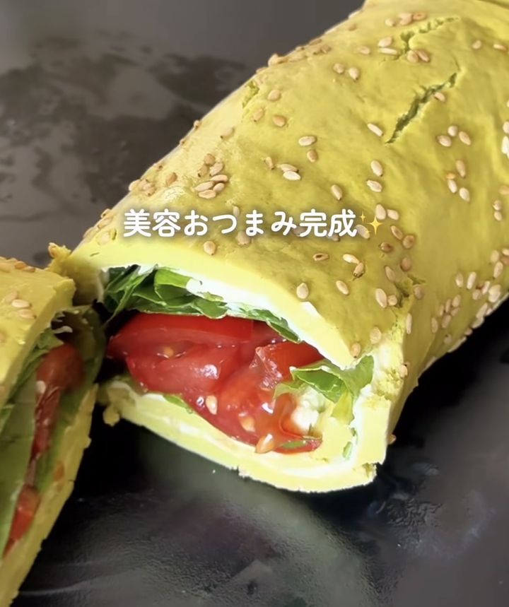 Sesame-covered yellow wrap cut in half revealing tomato, greens, and cheese inside.