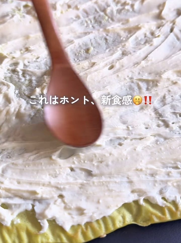 Close-up of a wooden spoon pressed into dough on a white textured surface, with a Japanese caption about a new texture.