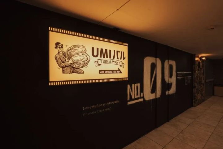 黒い壁に照らされた入口廊下に設置されたUMIバルFISH & WINEのレトロ調ロゴ看板とNO.09の大型グラフィックアートの店舗エントランス写真