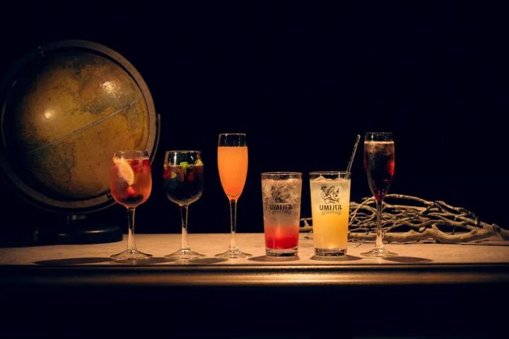 UMIバルのオリジナルカクテル5種の並び。サングリア・ブルーカクテル・ピンクスパークリング・グラデーションロング2杯をアンティーク地球儀とロープを背景に並べたドリンクラインナップ