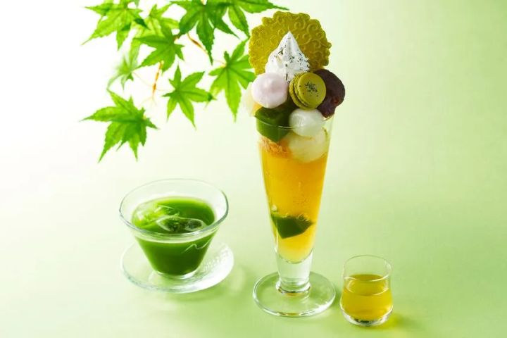 伊藤久右衛門の新茶パフェ全体像。抹茶ゼリー・マカロン・抹茶クッキーを盛り付けた縦長グラスと、付属の濃い緑色の抹茶ソースカップ・新茶ショットグラスをもみじを背景に並べた商品写真