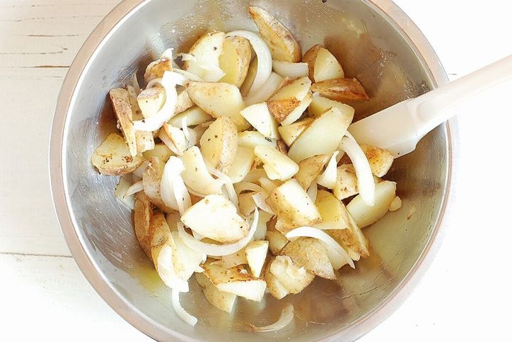 ステンレスボウルで焼いたじゃがいもと玉ねぎを調味料と混ぜている様子