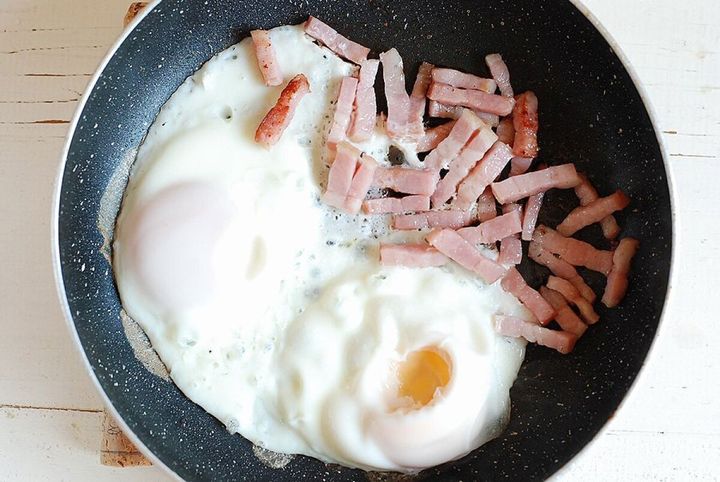 フライパンでカリカリのベーコンと半熟目玉焼きを焼いている様子