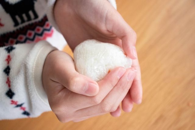 ラップで包んだおにぎりを握る手